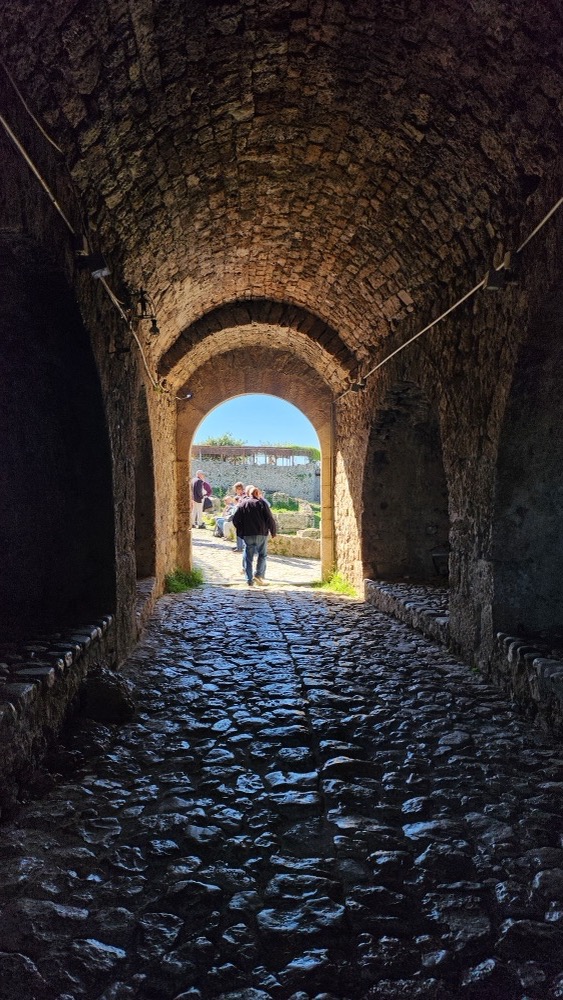 Looking out through the stone gateway tunnel of Krujë Castle towards the sunlit courtyard